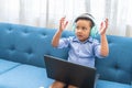 Little boy with raised hands using a laptop on a living room sofa Royalty Free Stock Photo