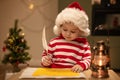 Little boy in red christmas hat writes letter to Santa Claus, Cute child writes a wish list at Christmas Royalty Free Stock Photo