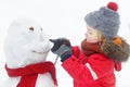 Little boy in red clothes having fun with big snowman. Active winter outdoor leisure for children. Child during stroll in a snowy Royalty Free Stock Photo