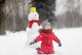 Little boy in red clothes having fun with big snowman. Child during stroll in a snowy winter park. Active winter outdoor leisure Royalty Free Stock Photo