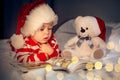 little boy in red hat reading book to teddy bear, merry christmas, winter holidays at home Royalty Free Stock Photo