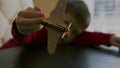 A little boy in a red sweater holds in his hands a wooden model of a toy airplane and plays with him at a table against