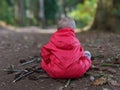 Little boy in a red waterproof sits in a mandala on the floor in the woods