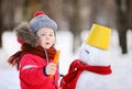 Little boy in red winter clothes having fun with snowman in snowy park Royalty Free Stock Photo