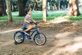 Little boy riding a blue bike in a dirty road in a forest park. Bicycle with the training wheels.