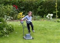 Little boy running with a lawn mower in the garden