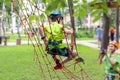 Little boy in safety equipment climbing on rope wall at adventure park. Fiend making a photo shot on smartphone. Children summer s Royalty Free Stock Photo