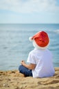 Little boy in Santa hat sitting on sand ocean