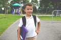 Little boy with school backpack and book in the play yard looking away from the camera