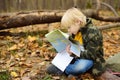 Little boy scout is orienteering in forest. Child is sitting on fallen tree and looking on map on background of teepee hut. Royalty Free Stock Photo