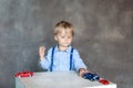 A little boy in a shirt with suspenders plays with toy multi colored toy cars. Preschool boy playing with toy car on a table at ho Royalty Free Stock Photo