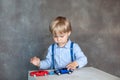 A little boy in a shirt with suspenders plays with toy multi colored toy cars. Preschool boy playing with toy car on a table at ho Royalty Free Stock Photo