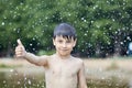 A little boy shows a thumbs up like in the middle of frozen water droplets in the air