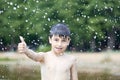 A little boy shows a thumbs up like in the middle of frozen water droplets in the air