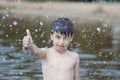 A little boy shows a thumbs up like in the middle of frozen water droplets in the air