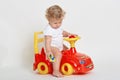 Little boy sit on red toy car and holding tiny vehicle in hands, looking on floor, barefoot child wearing bodysuit playing Royalty Free Stock Photo