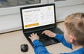 A little boy sits at a computer near the window