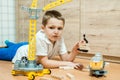 A little boy sits on the floor on a yellow background and plays with a toy yellow construction crane.