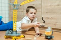 A little boy sits on the floor on a yellow background and plays with a toy yellow construction crane.