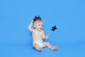 Little boy sits in front of a blue background. There is a black crown on his head, and in his hands he holds a magic wand in the Royalty Free Stock Photo