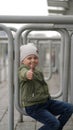 Little boy sits on an iron fence in a park and shows thumb