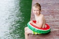 A little boy sits on the lake and plays with his feet in the water, a child`s rest in the village, a happy childhood Royalty Free Stock Photo