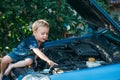 The little boy sits on the open hood of the car and examines the motor. A child studies the car and plays in the car Royalty Free Stock Photo