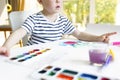 A little boy sits at a table and paints with bright colors on white paper. Royalty Free Stock Photo