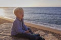 Little boy, sitting beach near sea, smiling