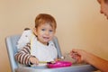 Little boy sitting at a chair for feeding and smiles. He holds a spoon in his hand and tries to eat himself from the plate Royalty Free Stock Photo