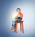 Little boy sitting on a chair with an open magic book, on blue background. Fairy tale concept Royalty Free Stock Photo