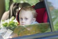 A little boy is sitting in a safety seat and looking out the open car window Royalty Free Stock Photo