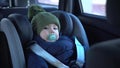 A little boy is sitting in a child seat in a car. A baby travels in a car in winter. Boy in jacket and hat. Royalty Free Stock Photo