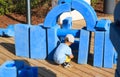 little boy is sitting on childrens playground in park with blue giant geometric figures for the development of imagination and Royalty Free Stock Photo