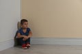 Little boy sitting in corner near yellow wall. Child in danger