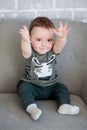 Little boy sitting on a gray sofa and pulling his hands up Royalty Free Stock Photo