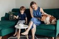 Little boy sitting on green modern sofa and having breakfast in living room, smiling woman playing and caressing cute Royalty Free Stock Photo