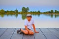 Little boy sitting on pier. Elementary age boy sitting on a wooden pier. Summer and childhood concept. Child on bench at the lake. Royalty Free Stock Photo