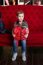 Little boy sitting on the red coach with christmas present in his hands Royalty Free Stock Photo