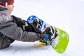 little boy sitting on snow putting his feet in snowboard bindings adjusting straps Royalty Free Stock Photo