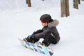 little boy sitting on snow putting his feet in snowboard bindings adjusting straps Royalty Free Stock Photo