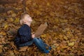 Little boy is sitting in wild forest in autumn leaves with book in hands. Children`s books about miracles and magic