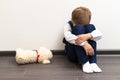 A little boy of six is offended and sits on the floor against a white wall next to a soft toy with his hands closed Royalty Free Stock Photo