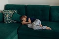 Little boy in sleepwear lying on big green modern sofa in living room and sucking finger. Bad habbit and manners of