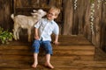 Boy smiles on wooden steps of the porch next to newborn goaling and hugs him