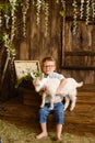 Boy smiles on wooden steps of the porch next to newborn goaling and hugs him