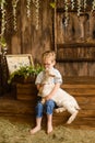 Boy smiles on wooden steps of the porch next to newborn goaling and hugs him