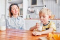 Little boy are smiling while having a breakfast in kitchen. Mom is pouring milk into glass Royalty Free Stock Photo