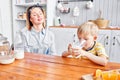 Little boy are smiling while having a breakfast in kitchen. Mom is pouring milk into glass Royalty Free Stock Photo