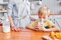 Little boy are smiling while having a breakfast in kitchen. Mom is pouring milk into glass Royalty Free Stock Photo